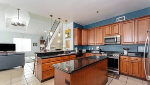 Una cocina moderna con armarios de madera, una isla grande, electrodomésticos de acero inoxidable y una escalera que sube a un nivel superior.