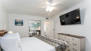 A hotel room with a bed, a TV, a ceiling fan, a dresser, and a painting on the wall.