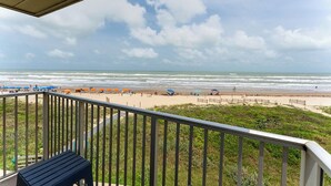 A balcony with a view of the beach, featuring umbrellas and people.