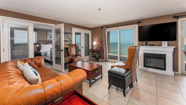 A spacious living room with a fireplace, leather sofas, a flat-screen TV, and a balcony with a view.
