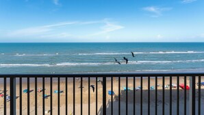 A beach with a railing, umbrellas, and people.