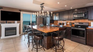 A modern kitchen with dark wood cabinets, a large island with bar stools, a built-in oven, and a flat-screen TV.