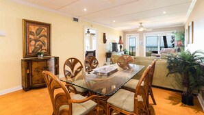 A dining area with a glass-top table, wicker chairs, and a decorative cabinet.