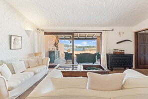 Un salon avec un canapé, une table basse et une vue sur la mer, visible à travers une porte vitrée.