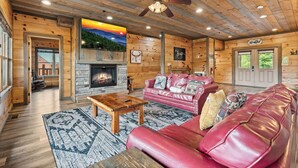 L’intérieur d’une cabane en rondins, avec une cheminée, un canapé en cuir, un plancher en bois et un ventilateur de plafond.