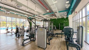 A gym with various exercise machines, large windows, and a green wall. - FIRST CLASS | 1BR | Elegant Comfort Awaits (Dubai South)