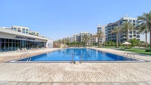 A swimming pool with a tiled deck, surrounded by palm trees and modern buildings. - FIRST CLASS | 1BR | Elegant Comfort Awaits (Dubai South)