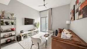 A modern living room with a sofa, coffee table, TV, and shelves with decorative items. - FIRST CLASS | 1BR | Elegant Comfort Awaits (Dubai South)