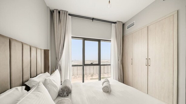 A hotel room with a large bed, a wardrobe, and a view of the desert through a large window. - FIRST CLASS | 1BR | Elegant Comfort Awaits (Dubai South)