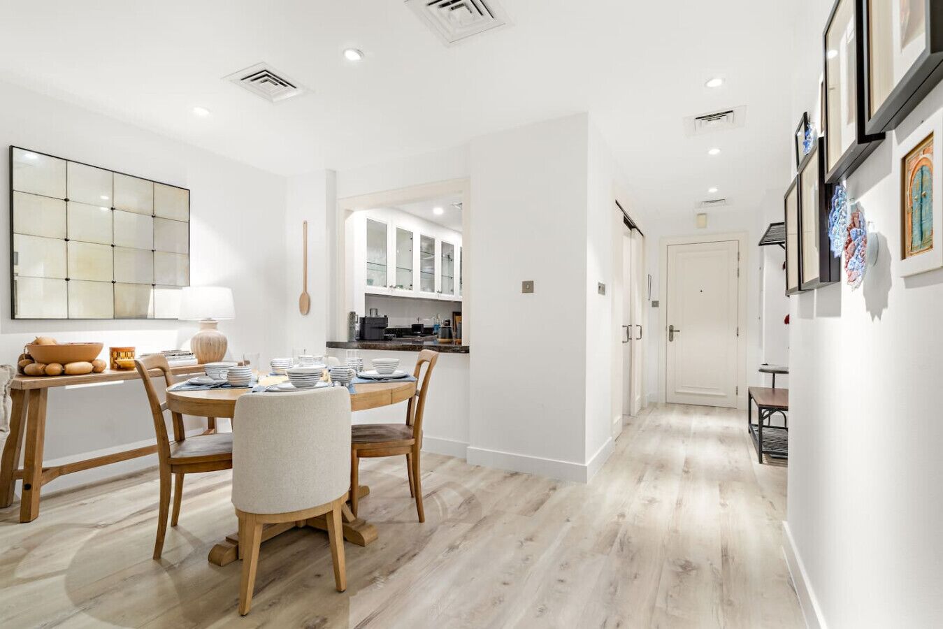 A modern kitchen with white cabinetry, a dining area with a round table and chairs, and a hallway with a door leading to another room.