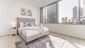 A modern bedroom with a large bed, bedside tables, a city view, and artwork on the wall.
