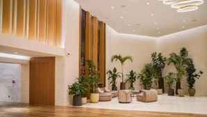 A spacious lobby with a wooden floor, a seating area with sofas and chairs, and several potted plants.