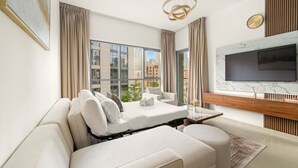 A modern living room with a sofa, a flat-screen TV, and a large window with a city view. - FIRST CLASS | 1BR | Burj Khalifa & Pool View (Downtown)