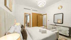 A modern hotel room with a large bed, bedside lamps, a marble dresser, a mirror, and a ceiling light fixture. - FIRST CLASS | 1BR | Burj Khalifa & Pool View (Downtown)