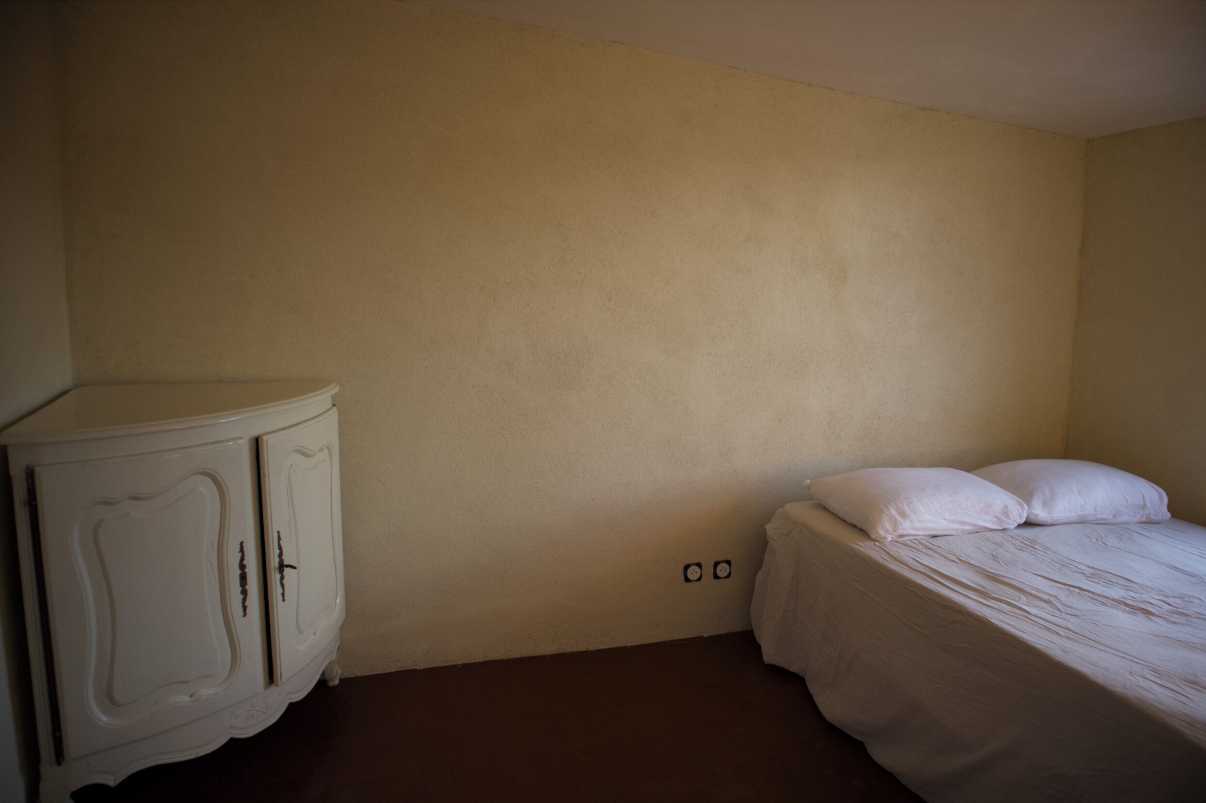 A room with a bed, a white dresser, and a plain wall.