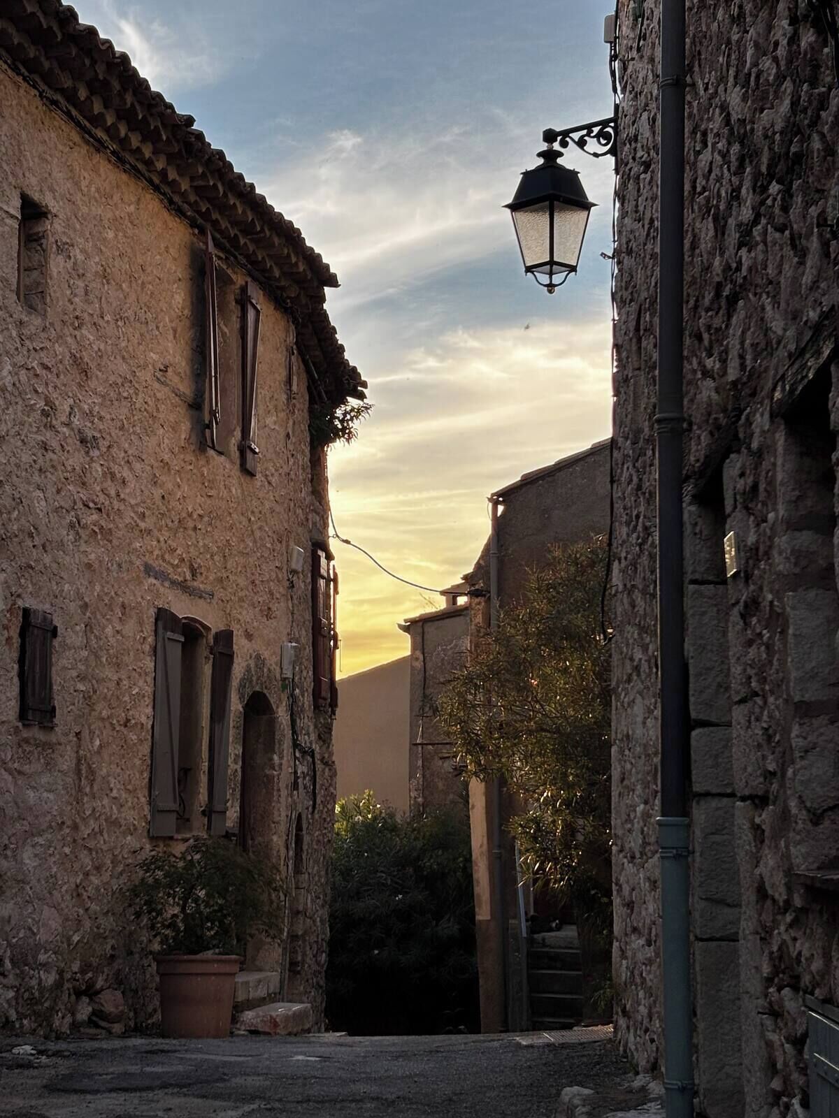 Une rue étroite bordée d’immeubles en pierre, un lampadaire et un pot de fleurs.