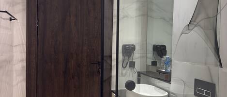 A modern bathroom with a dark wooden door, a glass shower enclosure, a white sink, and a toilet with a raised seat.