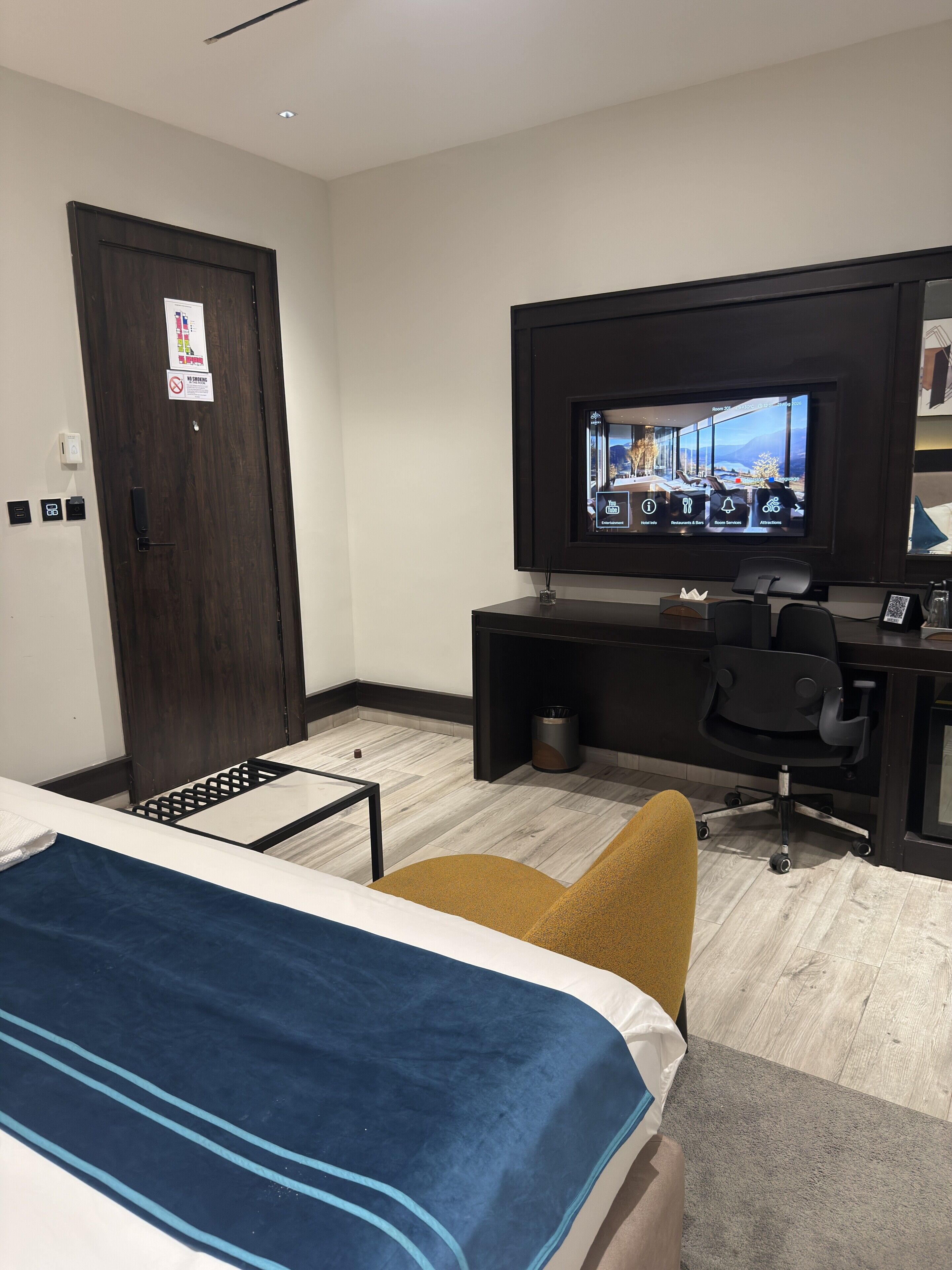 Una habitación de hotel con cama, un escritorio con silla, un televisor y una puerta.