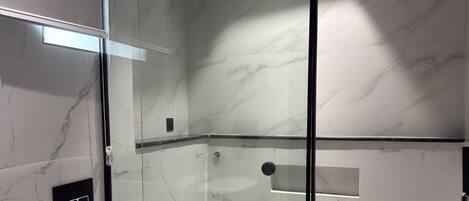 A modern bathroom with a glass-enclosed shower, a toilet, and a sink.