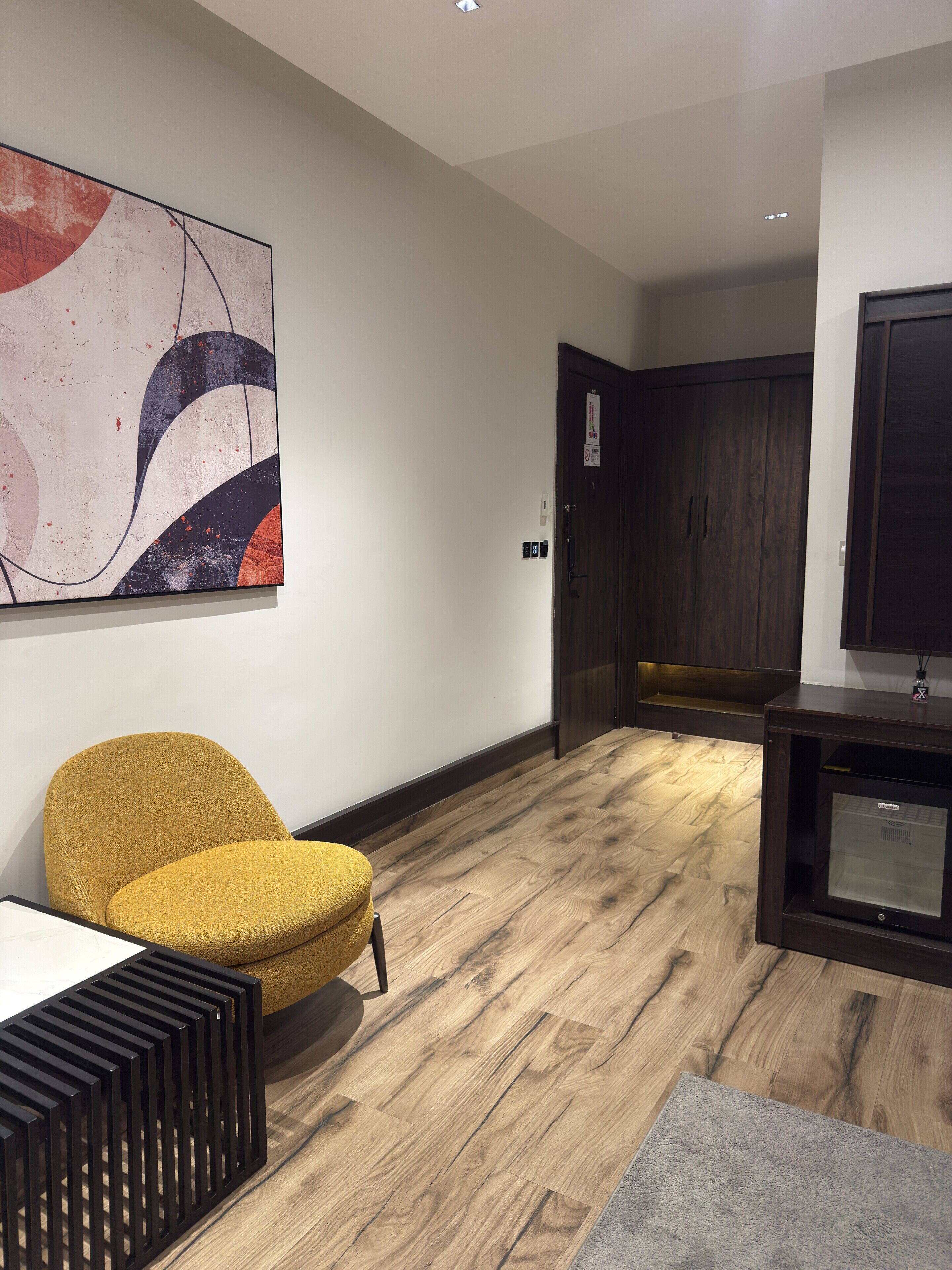 A modern interior with a wooden floor, a yellow armchair, a large abstract painting, and a dark wooden cabinet.