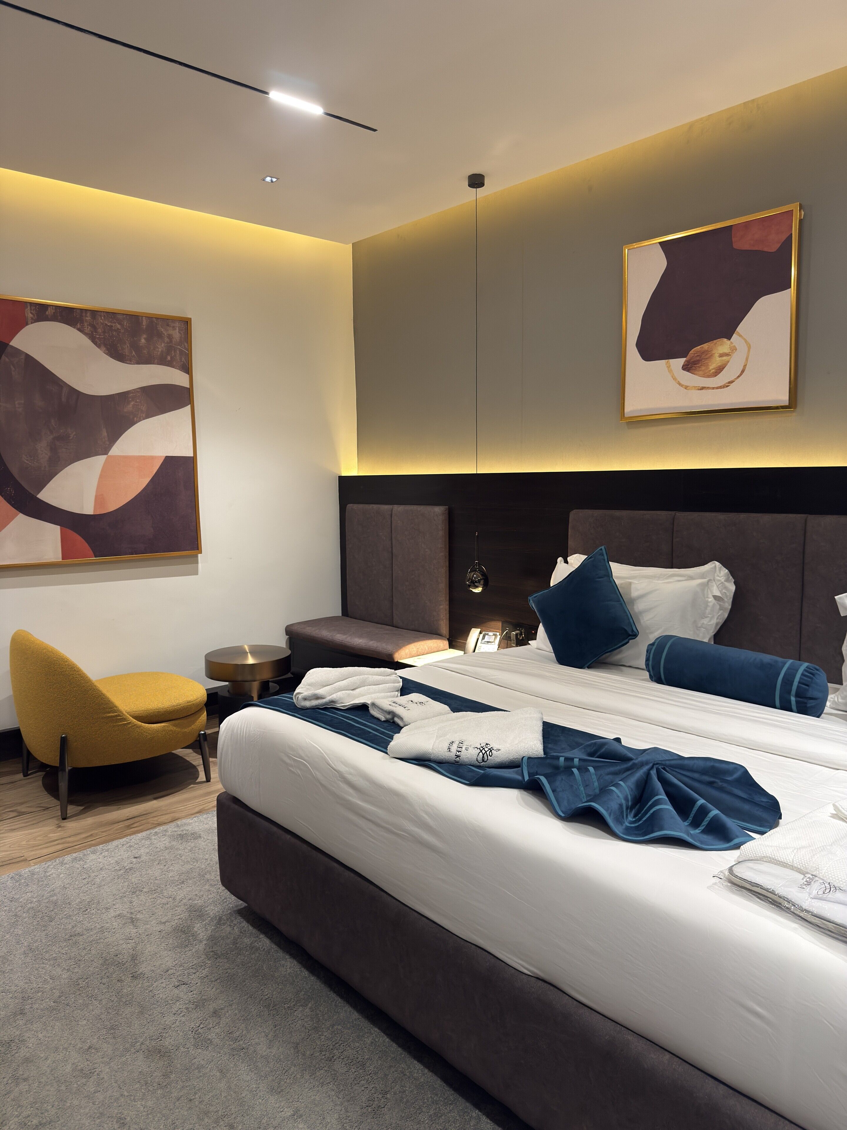 Une chambre d’hôtel moderne avec un grand lit, une table de chevet, une chaise et des œuvres d’art accrochées aux murs.