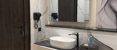 A modern bathroom with a marble wall, a wooden door, a white sink, and a large mirror.