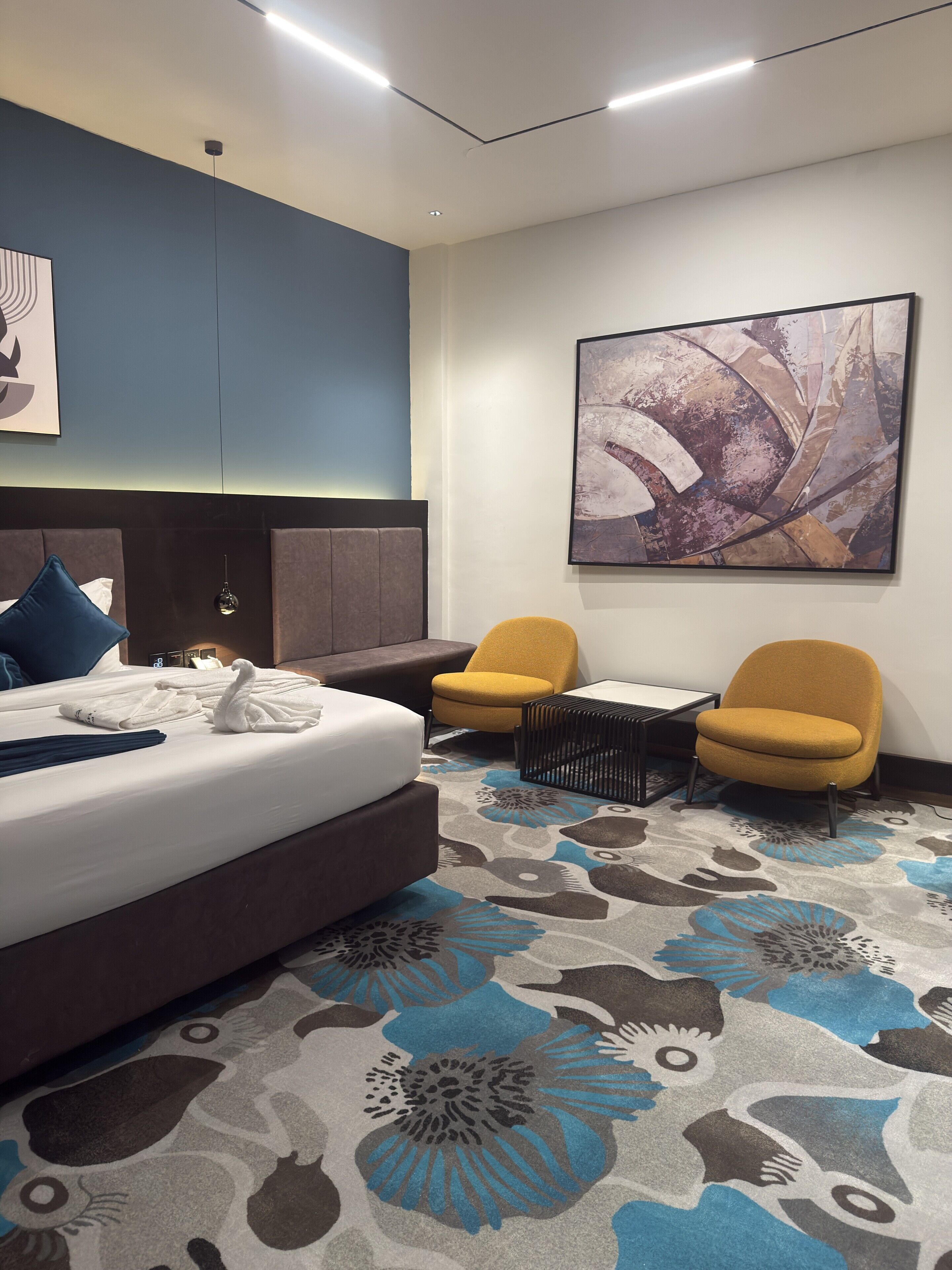 Habitación de hotel con una cama grande, dos sillones, una mesita de centro y un cuadro abstracto de gran tamaño en la pared.