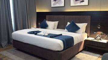 A modern bedroom with a large bed, two wall-mounted artworks, a bedside telephone, and a wooden floor.
