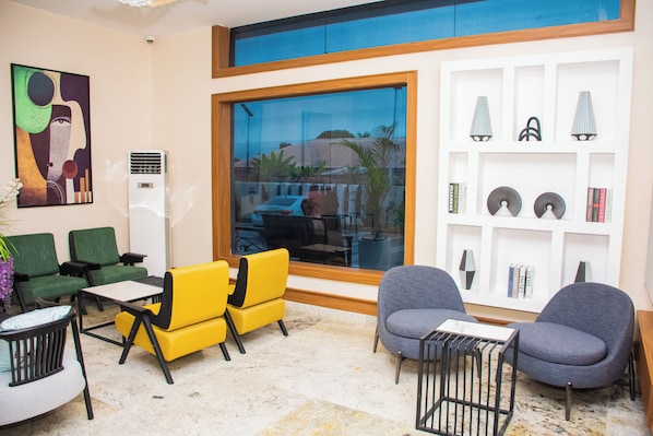 A modern lobby with green and yellow seating, a large window with a view, and a bookshelf with decorative items. - THE THRIBEKA INTERNATIONAL HOTEL (Asaba)