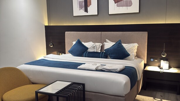 A modern hotel room with a large bed, a side table, a chair, and artwork on the wall. - THE THRIBEKA INTERNATIONAL HOTEL (Asaba)