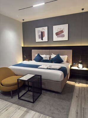 A modern hotel room with a large bed, a side table, a chair, and artwork on the wall. - THE THRIBEKA INTERNATIONAL HOTEL (Asaba)