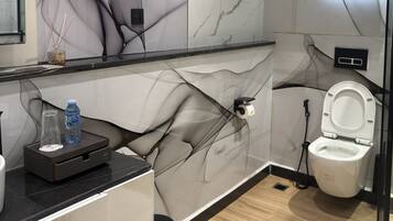 A modern bathroom with a marble wall, a toilet, a bidet, and a small counter with a water bottle.