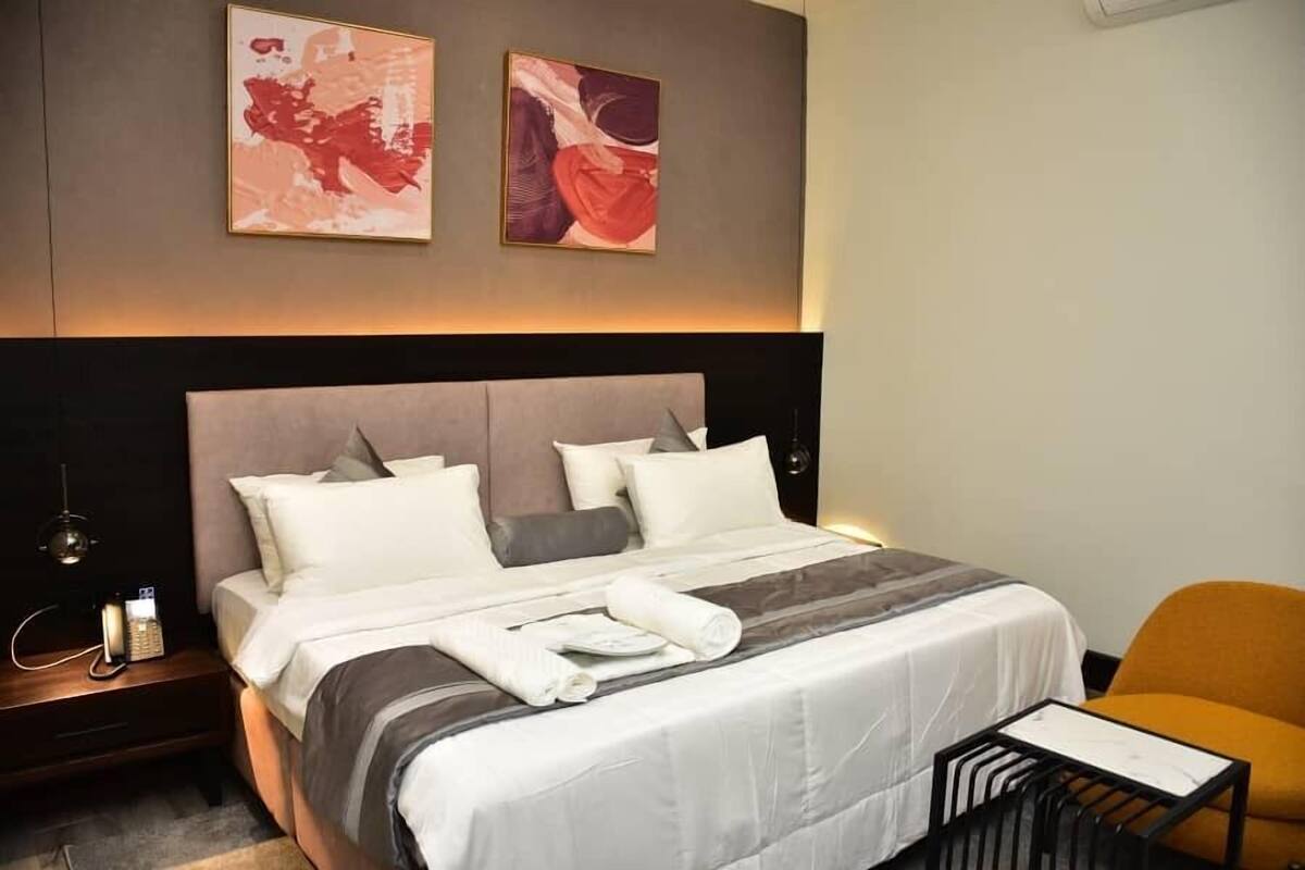 Une chambre d’hôtel moderne avec un grand lit, une table de chevet, une chaise et une œuvre d’art abstraite au mur.