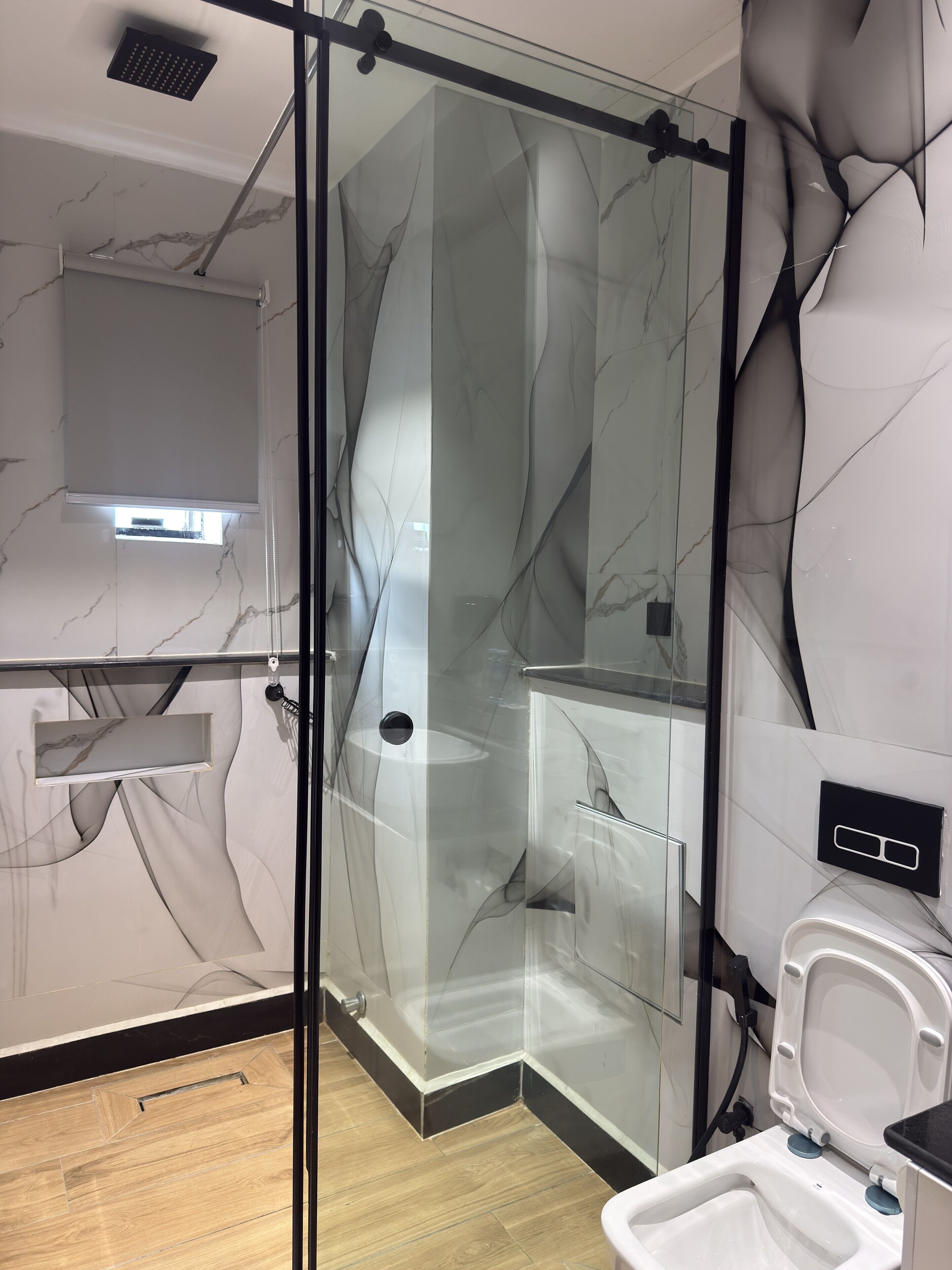 A modern bathroom with a glass shower enclosure, a toilet, and marble-patterned walls.