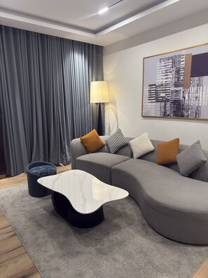 A modern living room with a grey sectional sofa, a white marble coffee table, a black lamp, and a cityscape painting on the wall. - THE THRIBEKA INTERNATIONAL HOTEL (Asaba)
