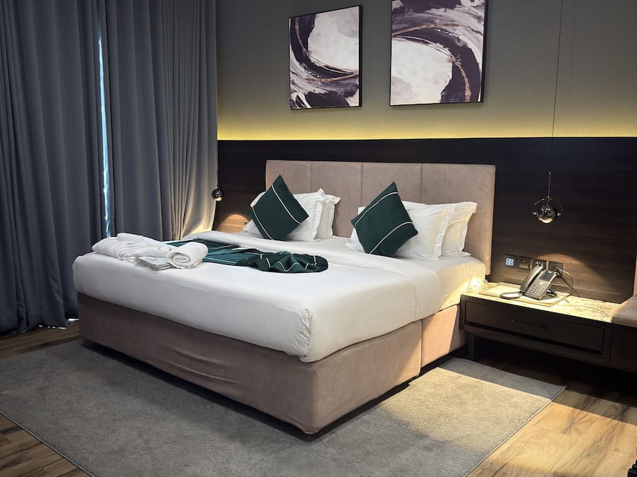 A modern hotel room with a large bed, a bedside table with a phone, and artwork on the wall.
