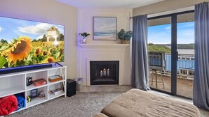 A living room with a TV, fireplace, and balcony with a view. - Cozy Pet-Friendly Condo w/ Pool (Osage Beach)