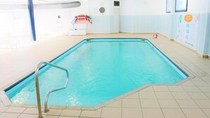 Una piscina interna con acqua cristallina, pavimento piastrellato e una scala in metallo.