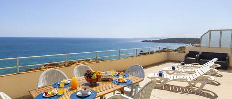 A terrace with a table set for breakfast, overlooking the sea.