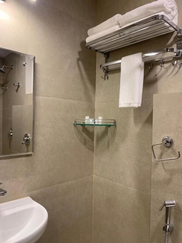 Un baño con lavamanos, espejo, toallero, estante de vidrio y ducha.