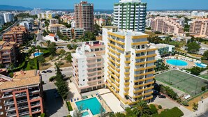 A high-rise hotel with multiple balconies, a swimming pool, and a tennis court. - Apartment pool sea view in Albufeira (Praia da Rocha)