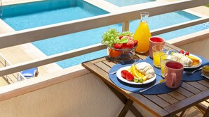 A poolside breakfast setup with fruit, juice, and a croissant on a wooden table. - Apartment pool sea view in Albufeira (Praia da Rocha)