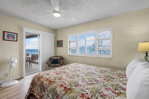 Ein Schlafzimmer mit einem Bett, einem Deckenventilator, einem Fenster mit Jalousien, einem Stuhl und einem Standventilator.