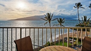 Een balkon met uitzicht op de oceaan, palmbomen en een berg in de verte.