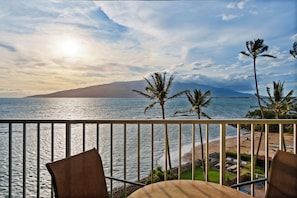 A balcony with a view of the ocean, palm trees, and a distant mountain. - 2-Bedroom Condo with AC, Ocean Views & Rooftop BBQ – Menehune Shores #509 (Kihei, Maui)