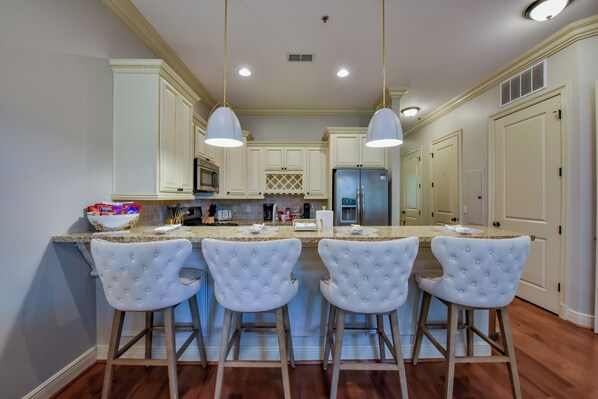 A kitchen with white bar stools, a central island, and a refrigerator.
