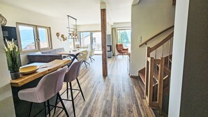 Une cuisine spacieuse avec une table à manger en bois, des tabourets de bar et une vue sur l’extérieur.