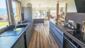 Une cuisine moderne dotée d’un îlot central, de planchers en bois et de grandes fenêtres offrant une vue sur l’extérieur.