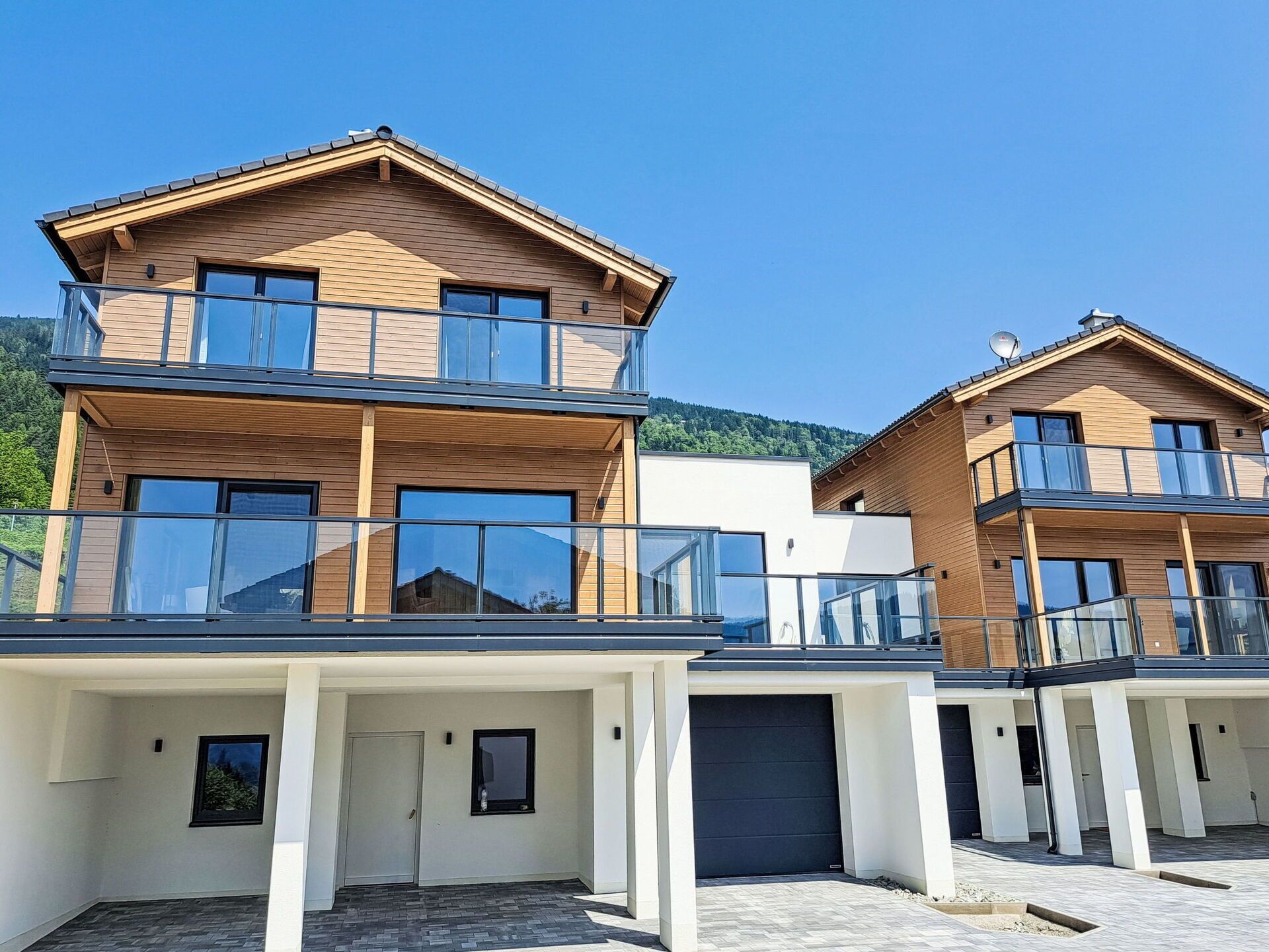 Un immeuble résidentiel moderne à deux étages, doté d’un balcon, de grandes fenêtres et d’un garage.