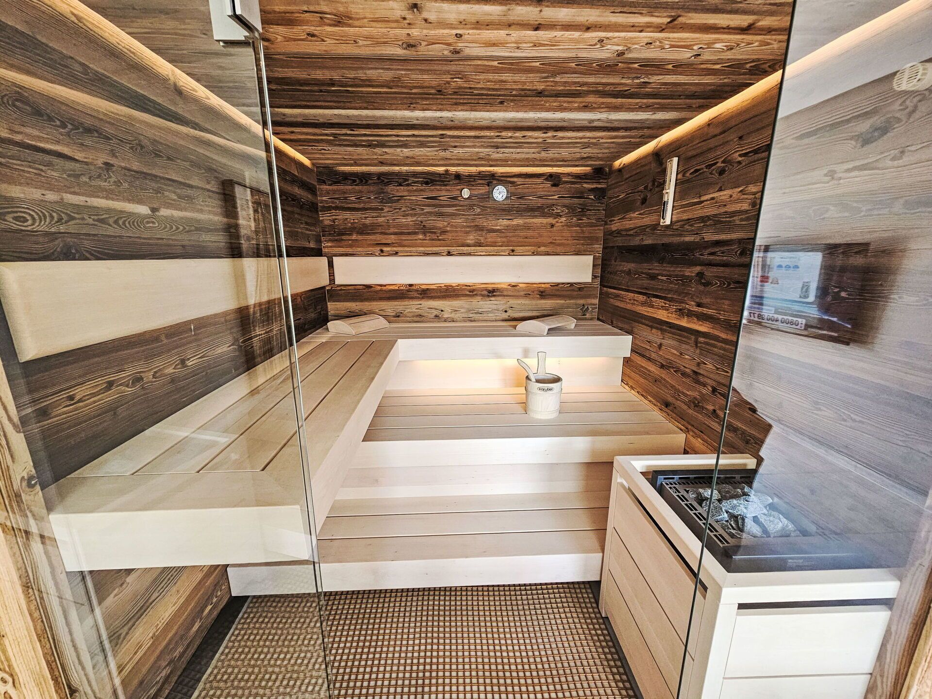 A sauna with wooden walls and a glass door, a bench, and a small table with a cup.